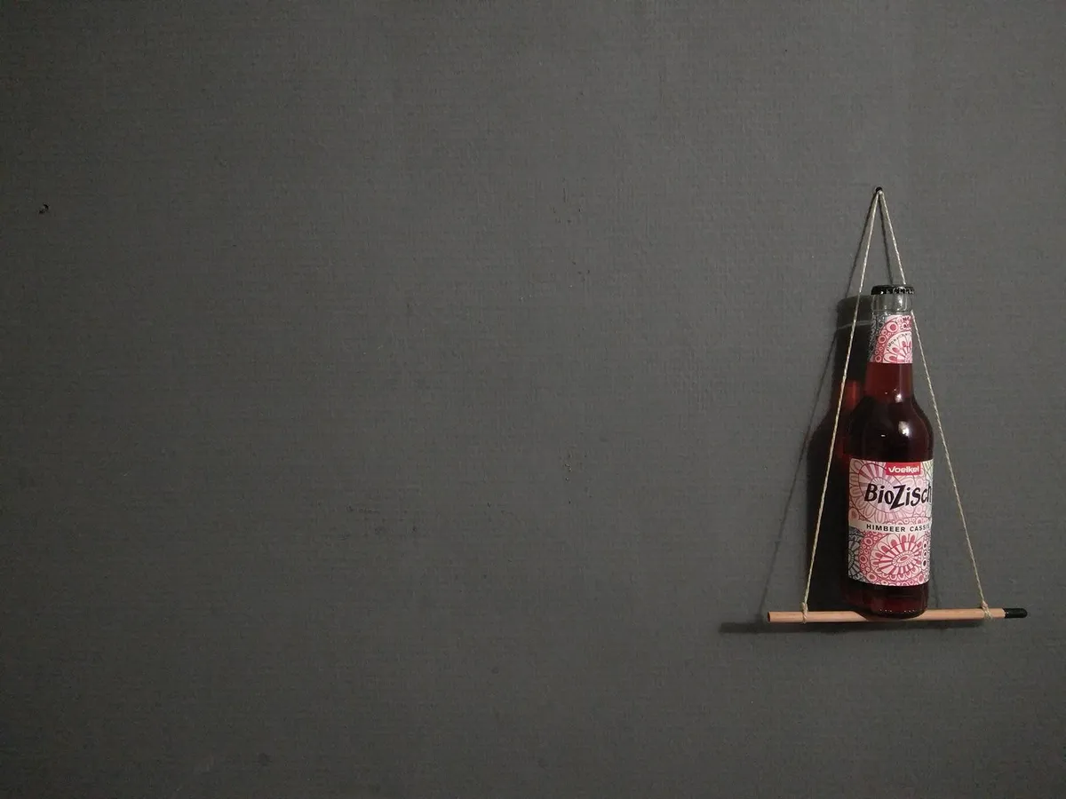 BioZisch Himbeer Cassis Flasche auf einem Mini-Bleistiftgestell vor grauer Wand