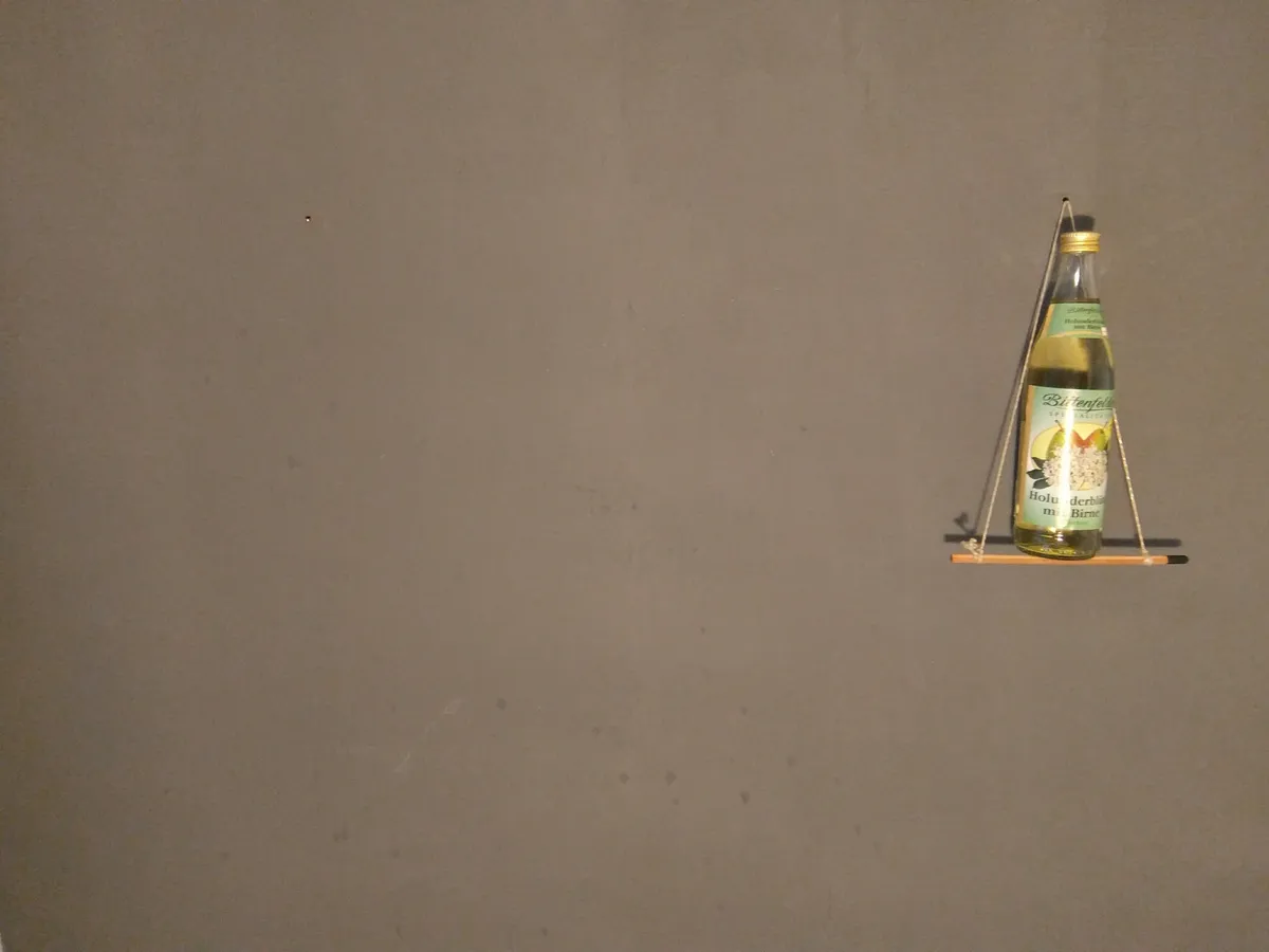 Flasche Bittenfelder Holunderblüten-Birne auf einem Mini-Bleistiftgestell vor grauer Wand