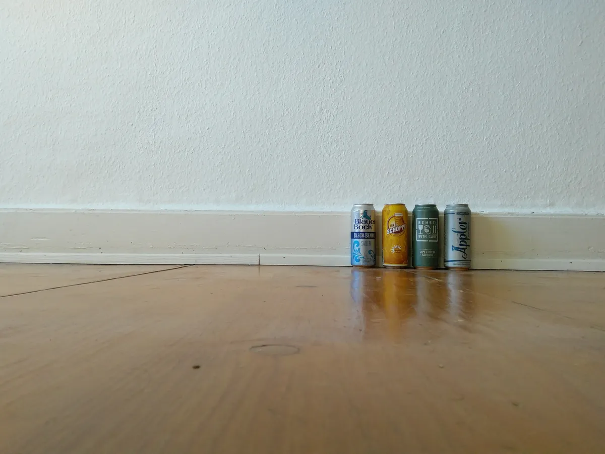 Vier Apfelwein-Dosen (Blauer Bock, my Schoppe, Bembel with Care, Äppler) nebeneinander auf einem Holzboden