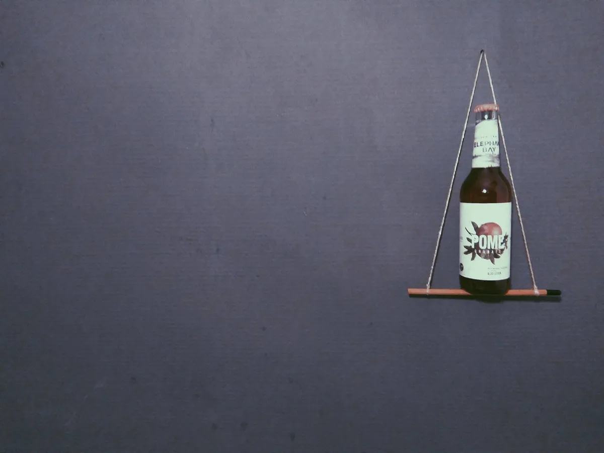 Flasche Elephant Bay Pomegranate Eistee auf einem Mini-Bleistiftgestell vor grauer Wand