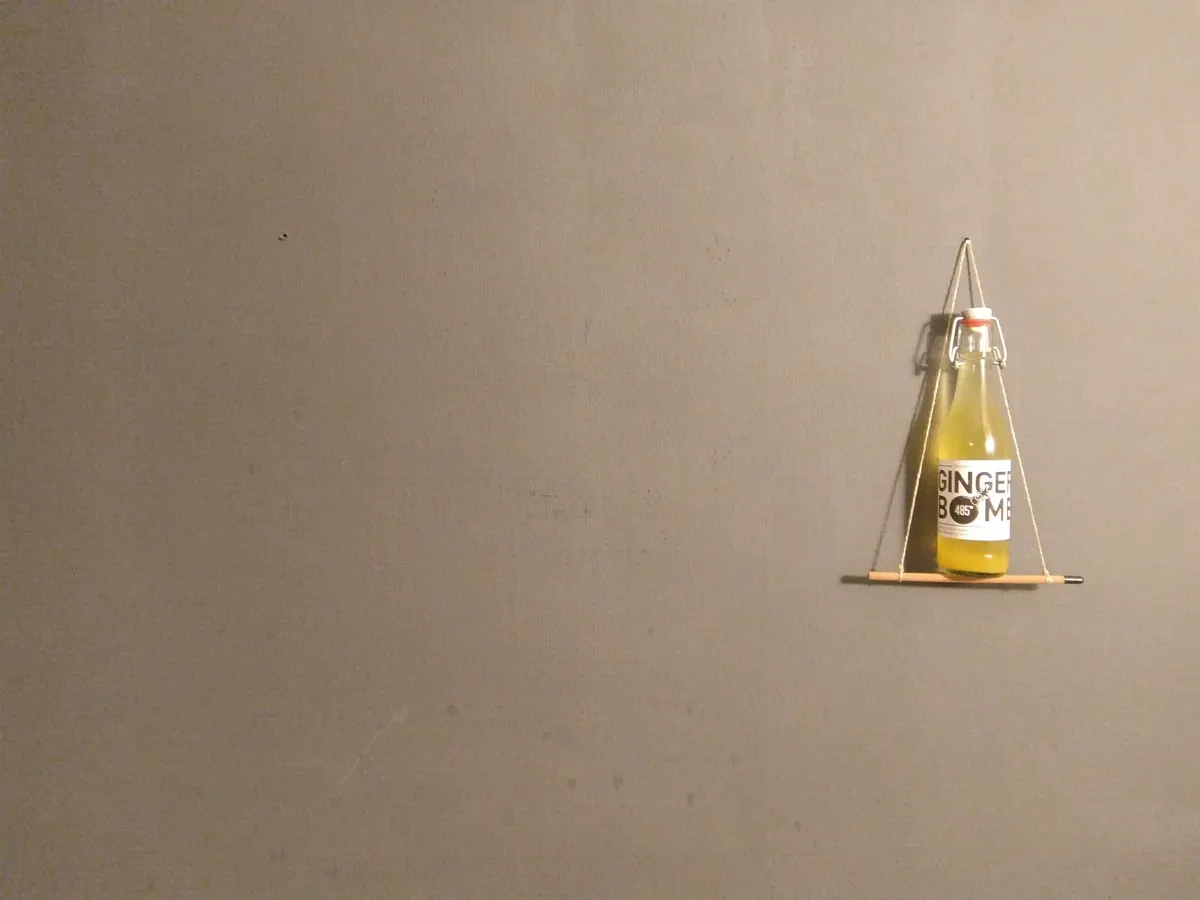 Flasche Ginger Bomb auf einem Mini-Bleistiftgestell vor grauer Wand